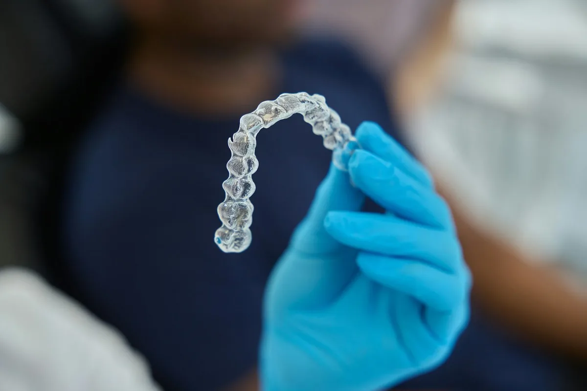 Alineador dental transparente sostenido con guante, listo para colocar